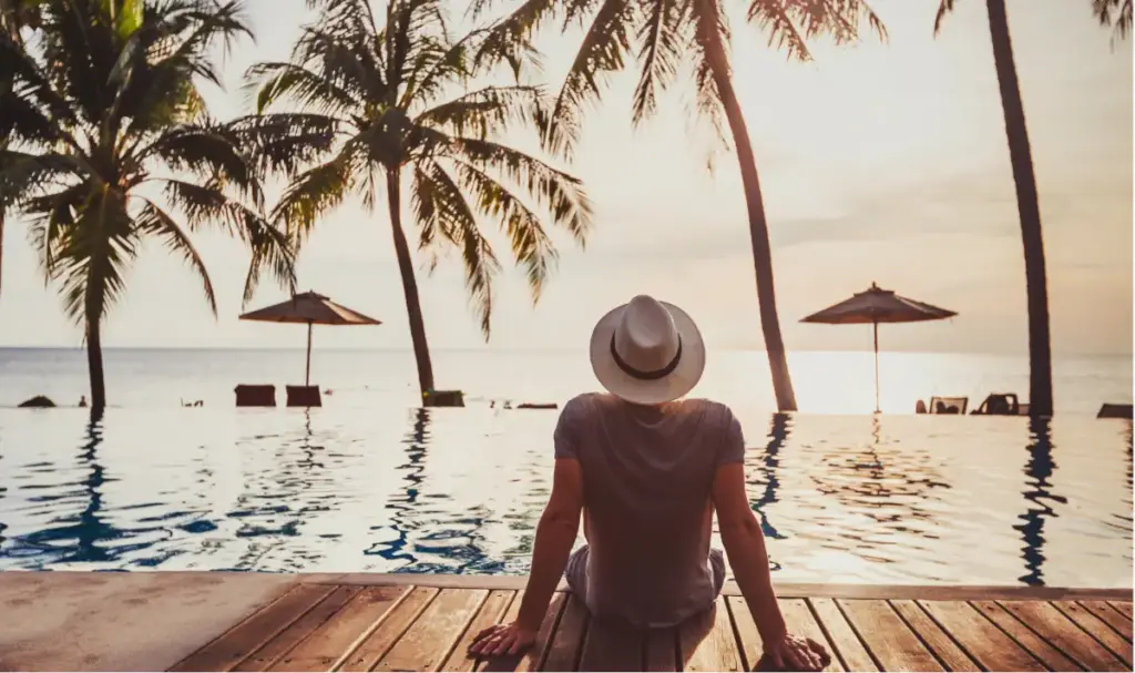 Person relaxing by an oceanfront infinity pool at sunset, representing luxury rehab and private addiction treatment.