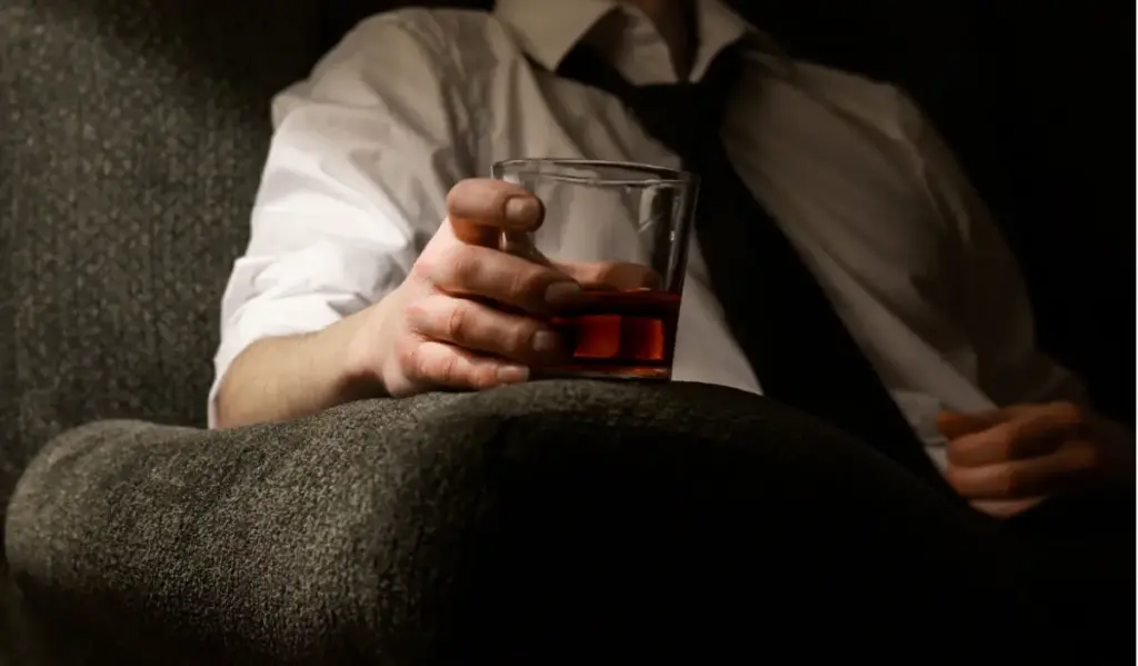 A person holding a glass of alcohol while sitting alone, symbolizing emotional struggle and substance use during addiction.