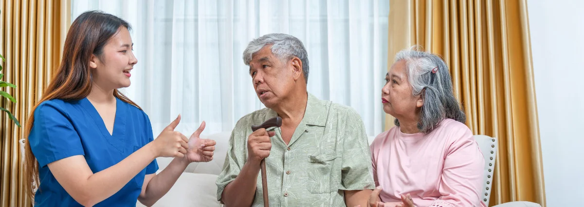 A professional counselor in blue scrubs engaging in a supportive aftercare planning session with an older couple in a comfortable home-like setting.