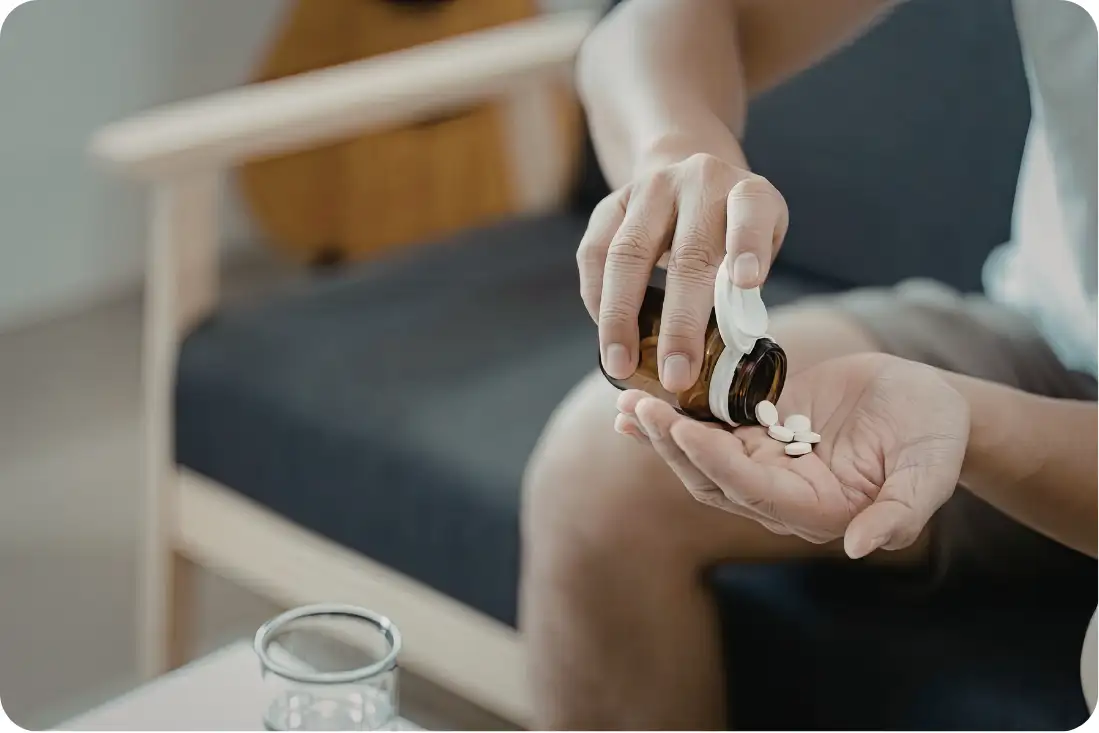A person pouring white medicinal tablets from a brown pill bottle into their palm.
